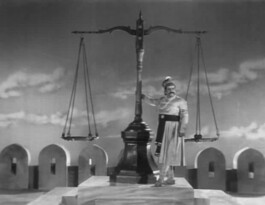 black and white film still showing a tall man in traditional south asian dress resting against a human sized set of weighing scales 