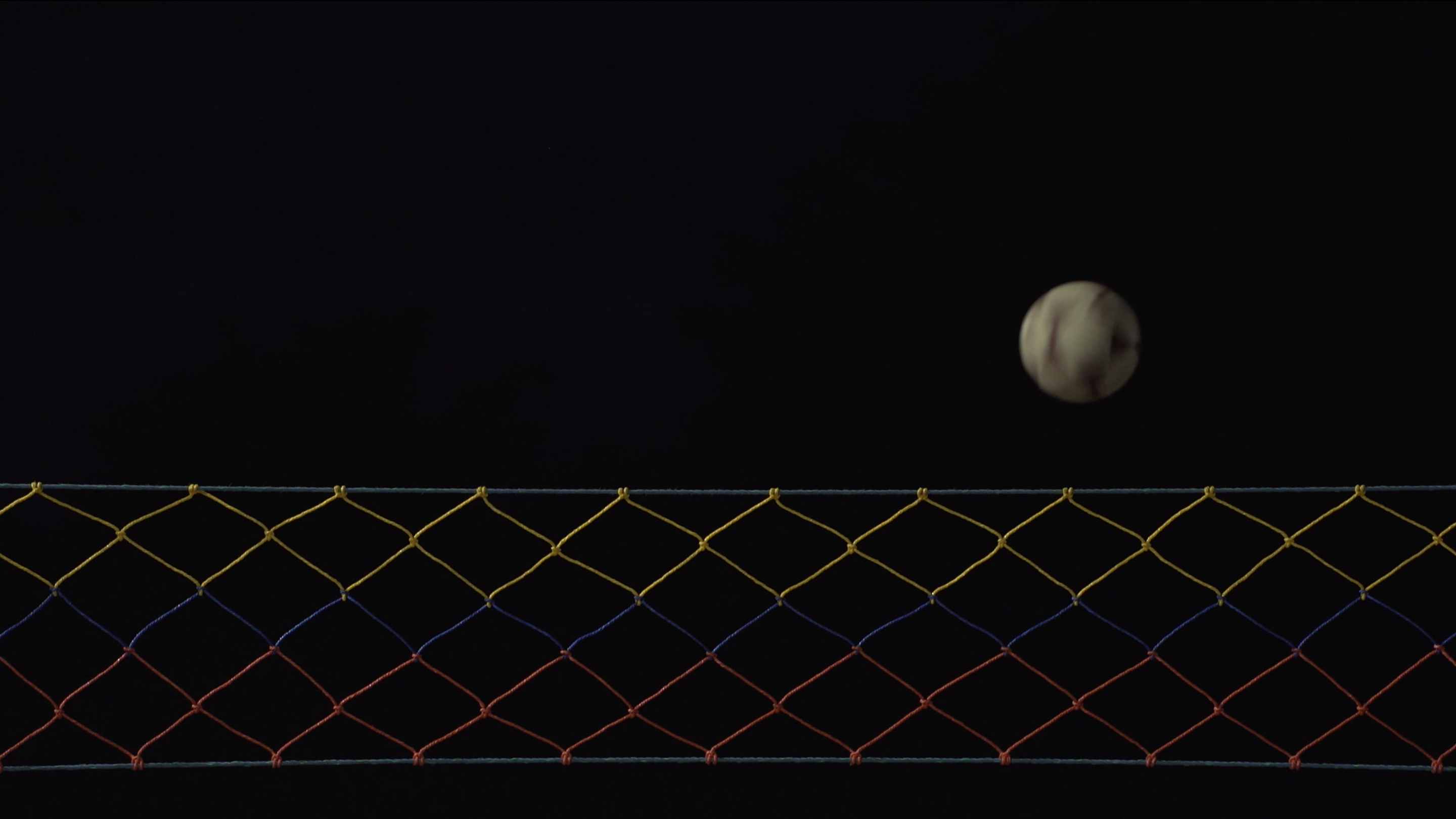 Nightime image of a volleyball net and ball mid-flight. It looks almost like the moon 